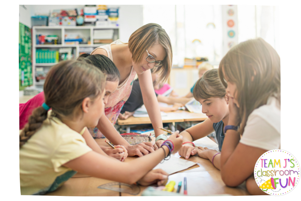 Photo of teacher standing and helping 4 students who are sitting.